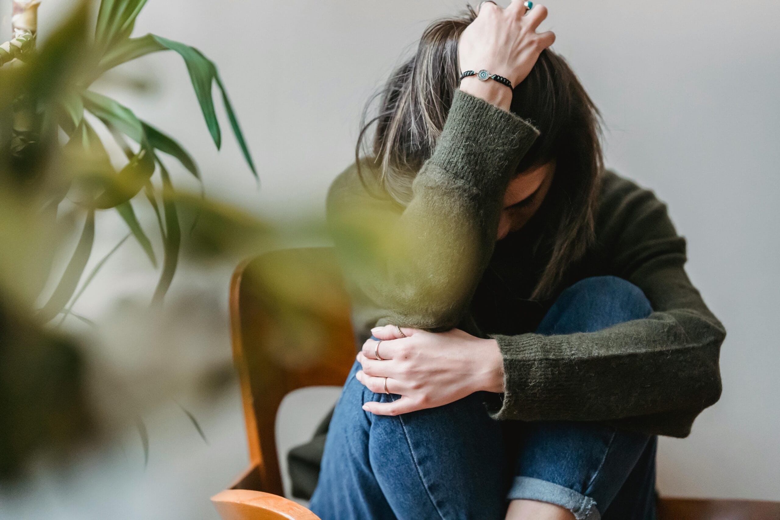 Reconocer la depresión sin miedo, es el primer paso Anonymous young sorrowed female in casual outfit touching dark hair and embracing knees while sitting on chair at home depresión